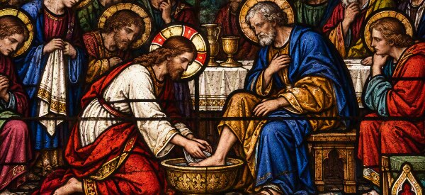 A richly colored Gothic stained-glass panel depicting Christ humbly washing a disciple's feet